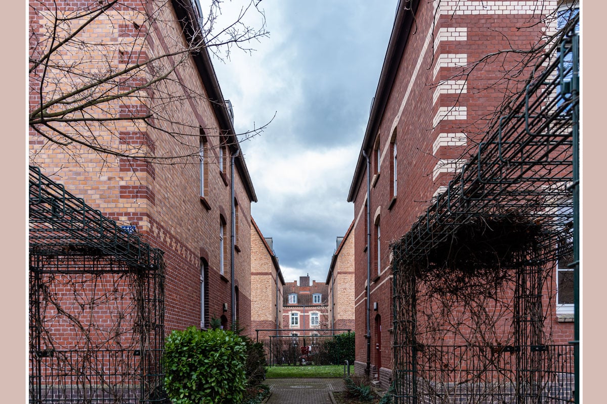 Blick durch die Häuserflucht/Gärten auf ein Gebäude der Parallelstraße